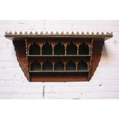 an old wooden shelf with decorative carvings on the top and bottom, against a white brick wall