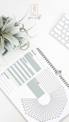 a white desk with a keyboard, mouse and plant on it next to a planner