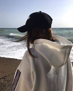 a person standing on the beach wearing a white jacket and black hat with waves in the background