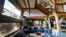 a living room filled with lots of furniture next to a tall wooden ceiling covered in windows