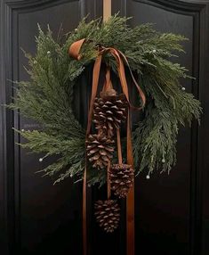 a wreath with pine cones and ribbons hanging from it's side on a door