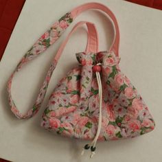 Pink Floral Drawstring Shoulder Pouch The pattern has pink flowers and green leaves on a pink background. The bag closes with a white cord through grommets and ends with one red and 2 green wooden beads. The bag closes with a drawstring and a snap at the top. The lining is all pink. There is one long cloth strap in pink and the pink flower pattern. The bag measures 9 x 3 x 10". Pink Rectangular Bucket Bag As Gift, Pink Rectangular Bucket Bag For Gift, Casual Pink Pouch Bucket Bag, Casual Handmade Pink Bucket Bag, Pink Adjustable Bag, Pink Flower-shaped Shoulder Bag As A Gift, Pink Flower-shaped Shoulder Bag For Gifts, Pink Flower-shaped Shoulder Bag As Gift, Pink Adjustable Shoulder Bag For Daily Use