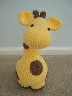 a crocheted stuffed giraffe sitting on the floor next to a wall