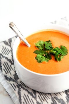 a white bowl filled with carrot soup and garnished with cilantro leaves