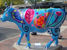 a colorful cow statue is on the sidewalk