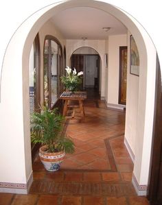 an archway leading into a house with potted plants on either side and benches in the middle