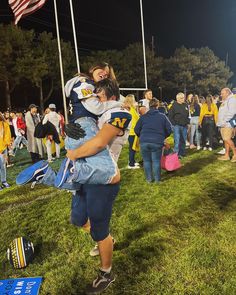 two people hugging each other in front of an american flag on a football field at night