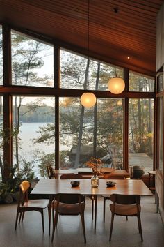 a dining room with large windows and wooden furniture on the floor, along with two lamps hanging from the ceiling