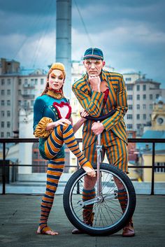 two people dressed as clowns standing next to each other on a unicycle