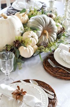 the table is set with white pumpkins, greenery and pine cones on it