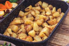 a pan filled with potatoes sitting on top of a wooden table next to carrots