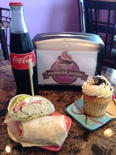 a sandwich and cupcake on a table next to a bottle of coca - cola