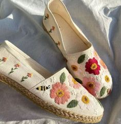 a pair of shoes with flowers painted on them sitting on a white cloth covered bed