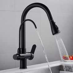 a black faucet with water running from it's spout and fruit in the sink