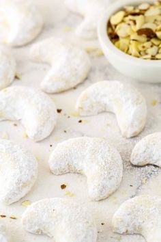 powdered sugar shaped cookies next to a bowl of nuts