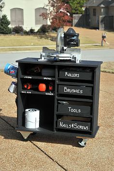 a black cabinet with lots of tools on it in the middle of a driveway next to a house