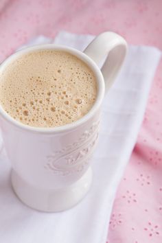 a cup of coffee sitting on top of a white table cloth next to a spoon