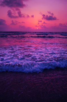 the sun is setting over the ocean with waves crashing in front of it and purple clouds