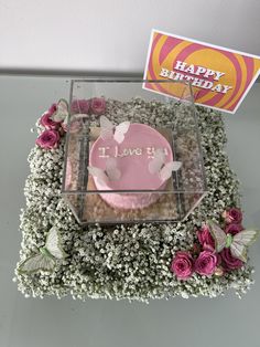 a pink frosted cupcake in a clear box surrounded by flowers and baby's breath