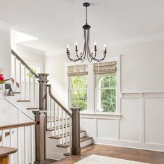 an empty living room with white walls and wood flooring, chandelier above the stairs