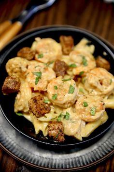 a black plate topped with pasta and shrimp