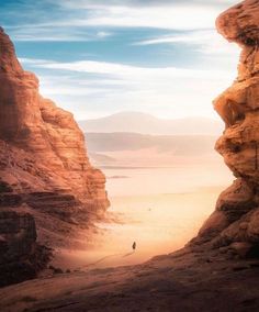 a person standing in the middle of a canyon between two large rocks, looking out into the distance