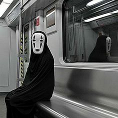 a person wearing a mask sitting on a subway train with their head covered by a black cloth