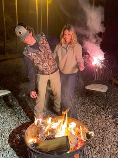 two people standing next to an open fire pit