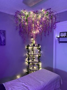 a bed with purple flowers hanging from it's headboard and lights on the wall