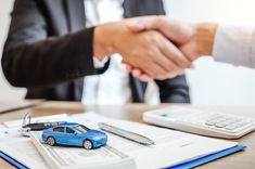 two people shaking hands over a car on top of a desk next to a calculator