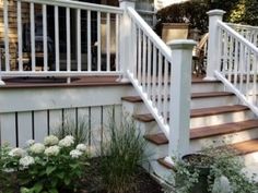 a porch with white railings and flowers on the ground next to steps leading up to a house