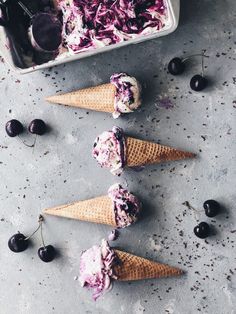 three ice cream cones with cherries in them on a gray surface next to an ice cream container