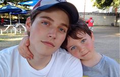 a man and boy sitting under an umbrella in the shade, posing for a photo