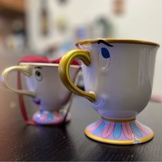 two coffee mugs with faces painted on them sitting on a table next to each other