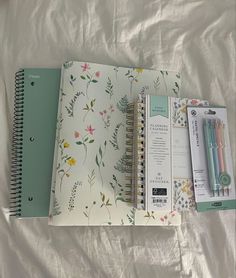 an open notebook and two pens sitting on top of a bed next to each other