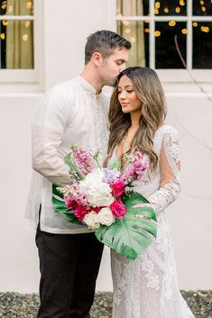 a bride and groom standing in front of a white building with lights on the windows