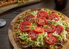 a pizza topped with lettuce and tomatoes on top of a wooden cutting board