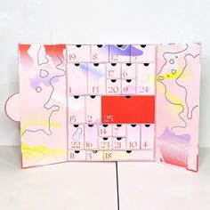 a pink and red calendar with hearts on it's cover is displayed in front of a white wall