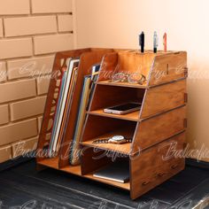 a wooden desk with books, magazines and pens on it in front of a brick wall