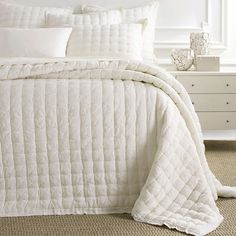 a bed with white comforter and pillows on top of it