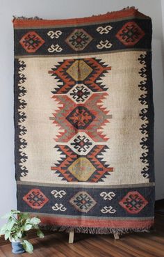 an old kilim rug is displayed on a wooden stand next to a potted plant