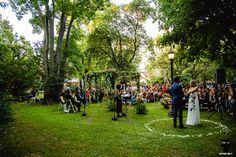 an outdoor ceremony in the middle of a park with lots of people sitting on lawn chairs