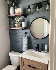 a white toilet sitting under a bathroom mirror next to a wooden sink vanity and shelf