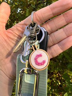 a hand holding a keychain with a pink letter on it