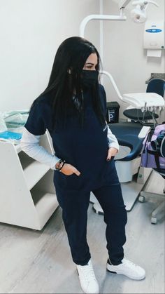 a woman standing in front of a dentist chair wearing a face mask and black sweatpants