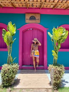 a woman wearing a hat standing in front of a colorful building with pink and blue doors