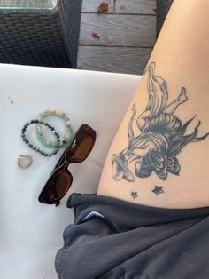 a woman's leg with a tattoo on it next to sunglasses and bracelets