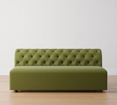 a green couch sitting on top of a hard wood floor next to a white wall