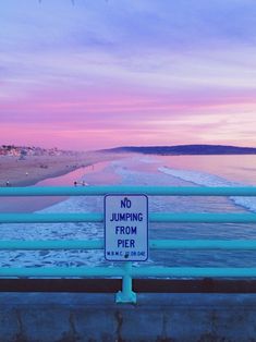 a no jumping from pier sign in front of the ocean at sunset or dawn with people walking on the beach