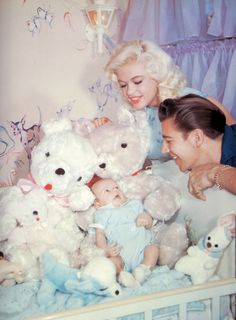 a man and woman are looking at stuffed animals in a crib with a baby